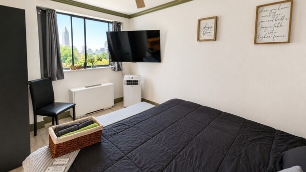 Una camera da letto con un letto, una TV, una ventola a soffitto, un termosifone e una finestra con tende.