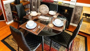 A dining area with a round table set for four, black chairs, and a fireplace in the background.