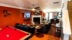 A pool table, leather sofas, a television, and a fireplace in a room with orange walls.