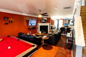 A pool table, leather sofas, a television, and a fireplace in a room with orange walls. - Gated Atlanta 3BR Gem | Private Community Pool (Atlanta)