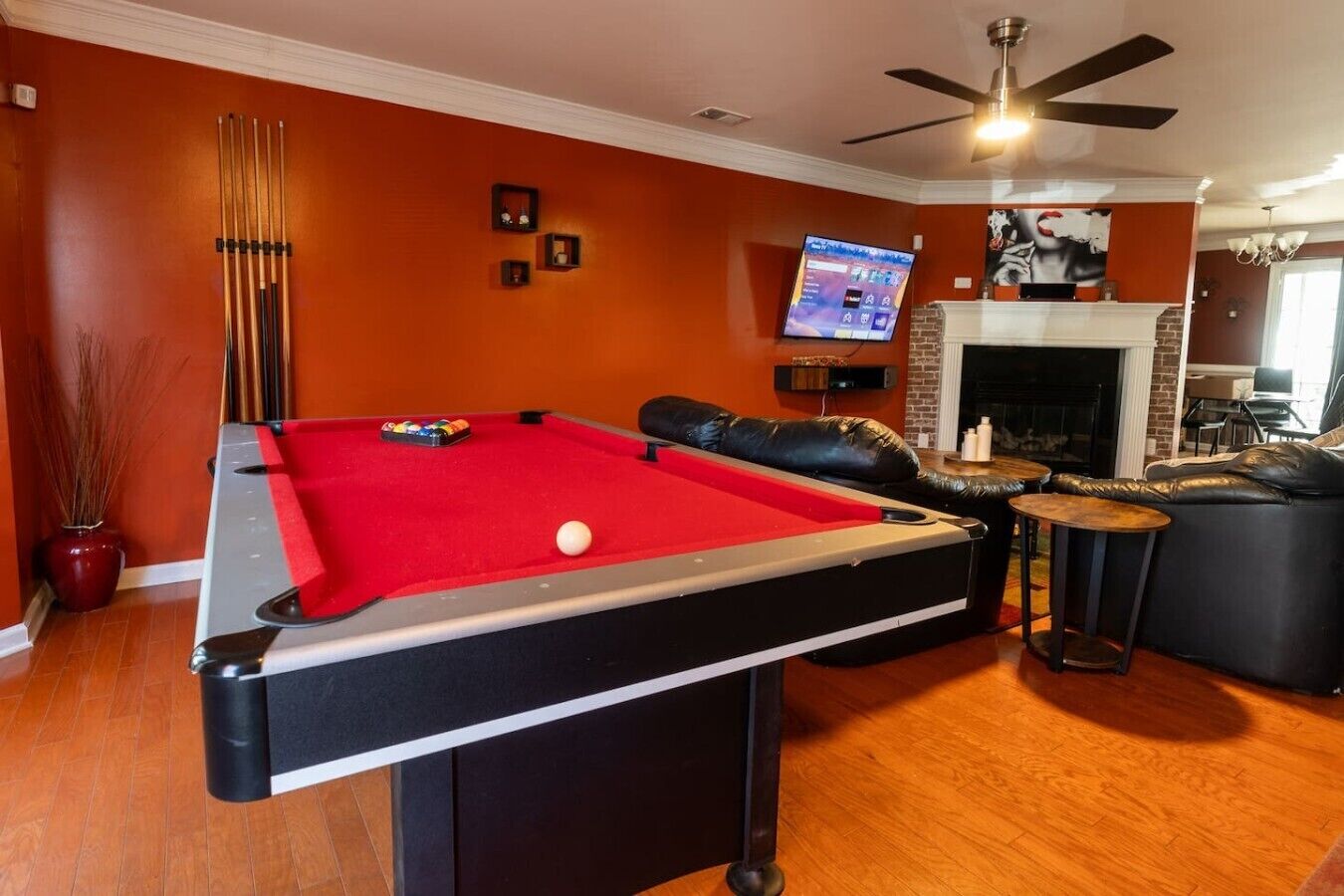 Une table de billard recouverte d’un drap de feutre rouge, un téléviseur fixé au mur et une cheminée en arrière-plan.