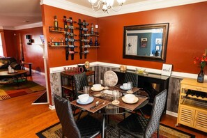 Un coin repas avec une table ronde dressée pour quatre personnes, entourée de chaises noires à revêtement en tissu. Un meuble à vin contenant des bouteilles est fixé au mur au-dessus de la table.