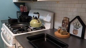 A kitchen with a gas stove, a kettle, a frying pan, a baking tray, a coffee-themed decoration, and a framed picture of a plant. - Downtown Atlanta 3BR Condo • Near Stadium & Arena (Atlanta)