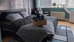 A bedroom with a bed, a wicker basket with slippers, a chair, and a radiator. - Downtown Atlanta 3BR Condo • Near Stadium & Arena (Atlanta)