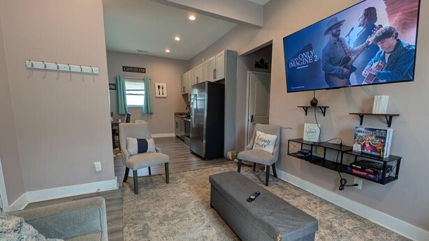 A living room with a TV, seating, and a kitchen in the background. - Cozy 4BR with Porch, King Bed Near Mercedez Benz & Downtown, Pet Friendly (Atlanta)