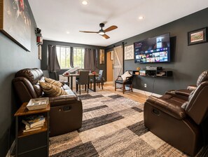 A modern living room with leather sofas, a flat-screen TV, and a dining area with a table and chairs. - Urban Comfort | King Beds & Movie Nights (Atlanta)