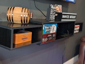 A shelf with a wooden barrel, a box of Dominoes, a 'Dirty Minds' magazine, and signs for 'Best Friends' and 'Movie Night'. - 2BR Urban Comfort 2 King Beds & Movie Nights (Atlanta)