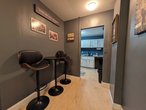 A hallway with a kitchen area, featuring a dining table with chairs, framed pictures on the wall, and a sign that reads 'trust me you can dance.' - Lux 2BR Condo w/ King Beds DTWN (Atlanta)