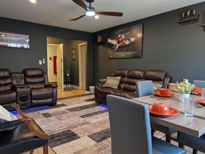 A modern living room with a dark wall, leather sofas, a dining table set, and a ceiling fan. - 2BR Urban Comfort 2 King Beds & Movie Nights (Atlanta)