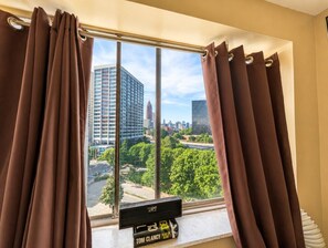 A window with curtains, a flat-screen TV, and a view of a cityscape with buildings and trees. - Beautiful 3BR Condo in DTWN Pool Access (Atlanta)