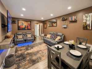 A modern living room with a sofa, a dining table set for four, and a flat-screen TV mounted on the wall. - Beautiful 3BR Condo in DTWN Pool Access (Atlanta)