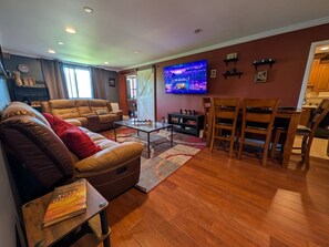 A living room with a sofa, a coffee table, a TV, and a dining area with chairs. - Lovely 2BR Condo WFH Heart of Downtown Pool Access (Atlanta)