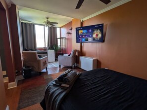 Ein Hotelzimmer mit Bett, Schreibtisch, Stuhl, Wandfernseher und einem fenster mit Vorhängen.