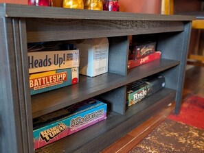 Estante de madeira com jogos de tabuleiro, incluindo Batalha Naval, Heads Up! e Risk.