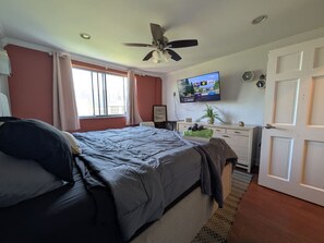 A bedroom with a bed, a ceiling fan, a TV, a dresser, and a door. - Lovely 2BR Condo WFH Heart of Downtown Pool Access (Atlanta)