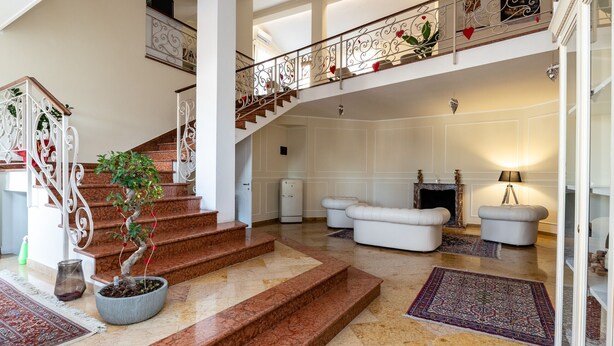 A grand staircase with ornate railings, a potted plant, and a fireplace in a spacious lobby area. - Scaligero Rooms Ida - Tosca - Rigoletto (Verona)