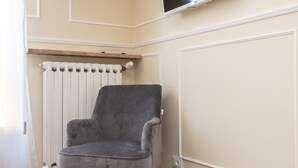A corner room with a grey armchair, a radiator, and a wooden shelf. - Scaligero Rooms Romeo (Verona)
