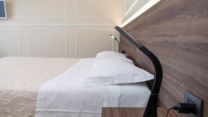 A neatly made bed with a white comforter and pillows, a wooden headboard with a built-in reading light, and a wall-mounted power outlet. - Scaligero Rooms Romeo (Verona)