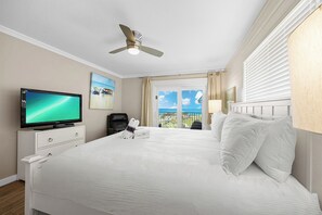 Ein Hotelzimmer mit Bett, Fernseher, Deckenventilator, Fenster mit Meerblick und einer Tür.