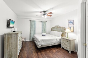 Ein Schlafzimmer mit Bett, Nachttisch, Kommode, Deckenventilator und Kunstwerken an den Wänden.