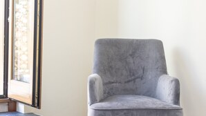 Un fauteuil gris dans une pièce avec une fenêtre, un plancher foncé et un mur blanc.