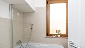 Une salle de bain moderne avec une douche à parois de verre, une baignoire blanche et une fenêtre à cadre en bois agrémentée d’une plante.