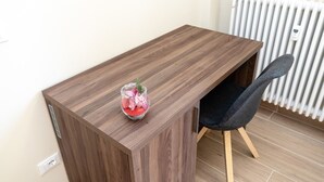 Un bureau en bois, un récipient en verre contenant des objets roses, une chaise et un radiateur.