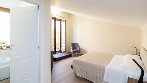 Une chambre à coucher avec un lit, une chaise et une salle de bain visible à travers une porte ouverte.