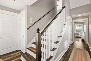 Eine moderne Treppe mit weißen Geländern und Holzstufen, die zu einem Flur mit einem gemusterten Teppich führt.