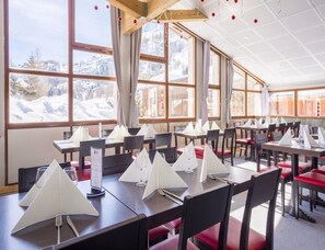 A restaurant with multiple tables, each set with white napkins, glasses, and cutlery. Large windows offer a view of a snowy landscape. - Chic Triple Retreat With Playstation (Tignes)