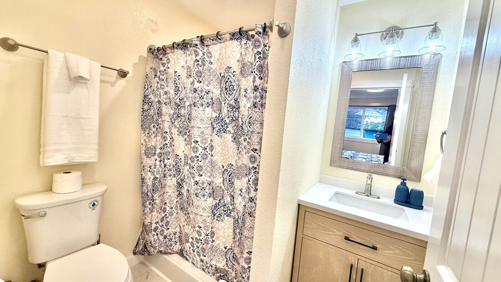 A bathroom with a toilet, a shower curtain, a sink with a mirror, and a towel hanging on the wall.