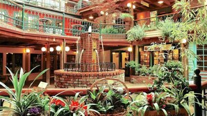 Ein mehrgeschossiges Atrium mit einer zentralen Backsteinbrunnen, umgeben von Topfpflanzen und einem Café und einer Kneipe.