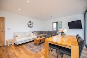 Een moderne woonkamer met een bank, salontafel, eettafel en een aan de muur bevestigde televisie.