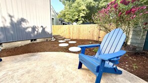 A blue Adirondack chair on a concrete patio with stepping stones leading to a wooden fence.