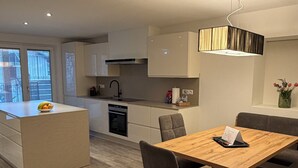 Una cocina moderna con una isla central, un comedor con mesa y sillas de madera, y vistas al exterior a través de un ventanal amplio.