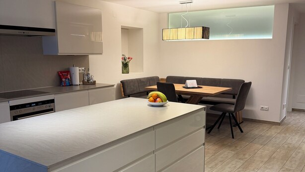 Una cocina moderna con una isla central, un área de comedor con mesa y sillas, e iluminación empotrada en el techo.