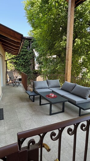 Ein überdachter Außenbereich mit einer Sitzecke, einer Couch und Sesseln, einem Tisch und einer Pergola.