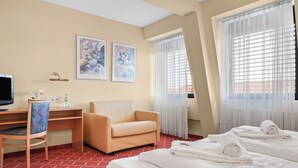 A hotel room with a bed, a desk with a chair, a television, and two framed artworks on the wall.