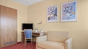 A hotel room with a desk, chair, TV, and two framed artworks on the wall.