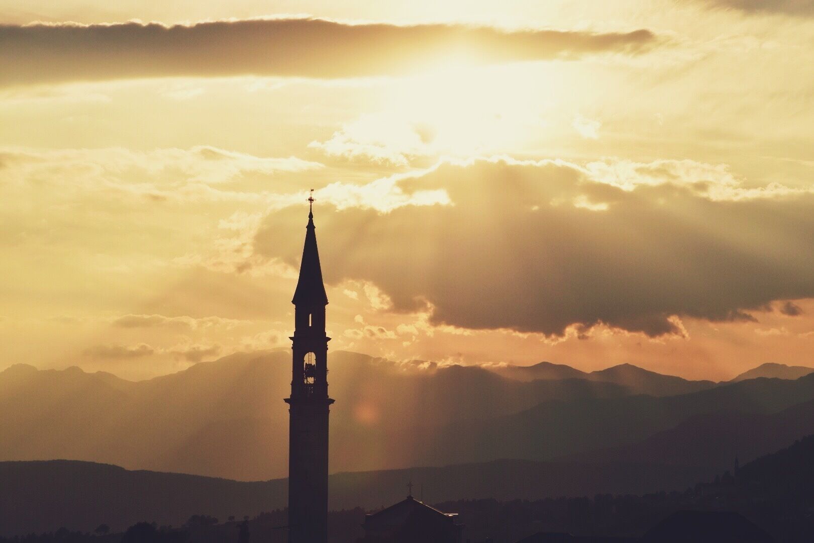 Le clocher d’une église se détache sur le ciel au coucher du soleil, avec des montagnes en arrière-plan.