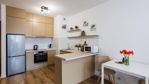A compact kitchen with a refrigerator, oven, microwave, and wooden flooring. - Malila Apartments Łaszkiewicza 8 (Kraków)
