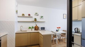 A modern kitchen with a central island, wooden cabinets, and a dining area with a table and chairs. - Malila Apartments Łaszkiewicza 8 (Kraków)