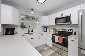 A modern kitchen with white cabinets, a stainless steel refrigerator, a microwave, a stove, and a coffee maker. - NEW Saltwater Pool 3br near the beach! (Clearwater)