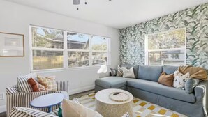 Ein Wohnzimmer mit grauem Sofa, einem gestreiften Sessel, einem runden Couchtisch und Tapete mit Muster.