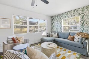 A living room with a grey sofa, striped armchair, round coffee table, and patterned wallpaper. - NEW Saltwater Pool 3br near the beach! (Clearwater)