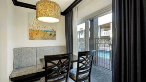 Una stanza con un divano, due poltrone, un tavolo, una lampada a sospensione e vista su una piscina attraverso una porta in vetro.