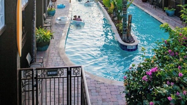 Area piscina con uno scivolo acquatico, circondata da edifici con balconi e piante in vaso.
