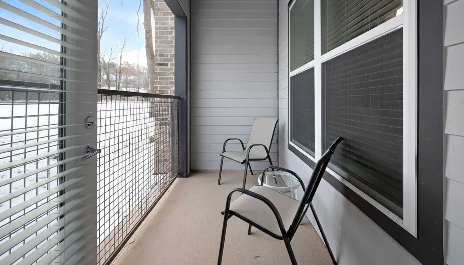 Un balcon avec une balustrade en métal, deux chaises et une fenêtre avec des stores.