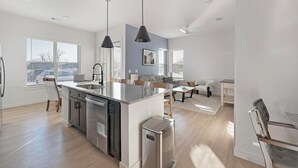 Une cuisine moderne dotée d’un îlot central, d’appareils électroménagers intégrés et de luminaires suspendus.