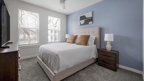 A bedroom with a bed, nightstands, a TV, and a window with blinds. - Landing | Modern 1BD, Yoga Studio, Clubhouse (Little Rock)